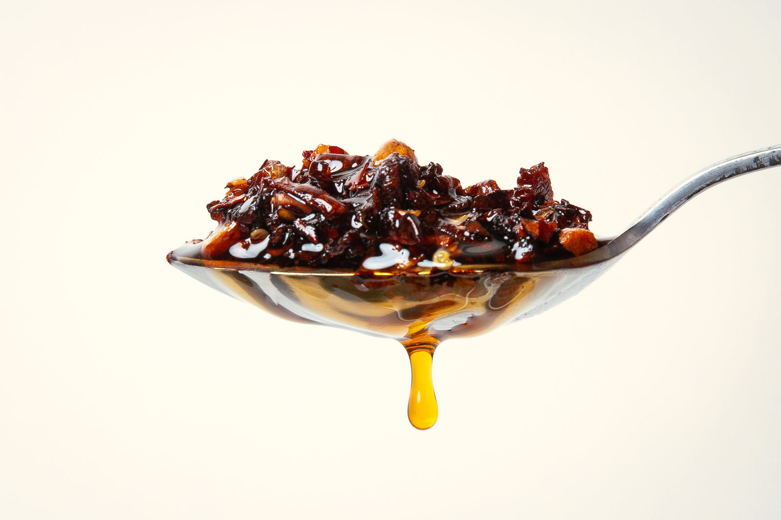 A spoonful of chili crisp with chili oil dripping from it